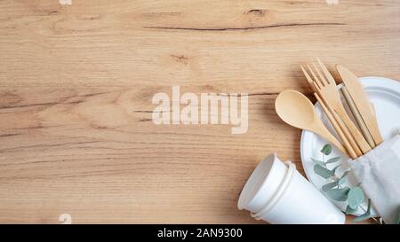 Reusable eco natural bamboo utensils cutlery with biodegradable paper cups and plate on wooden table. Top view, flat lay, copy space. Zero waste, plas Stock Photo