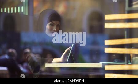 Beautiful Muslim female sitting in cafe, using shopping app on tablet, banking Stock Photo