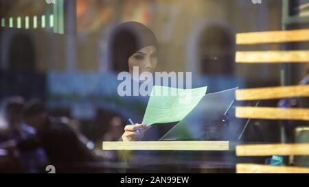 Self-confident Arabic business lady in cafe looking through documents, freedom Stock Photo