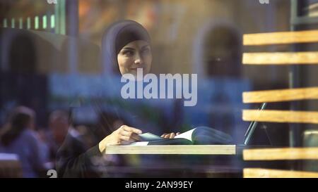 Attractive female student in traditional arabic clothing reading book in cafe Stock Photo