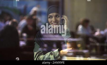Attractive young Arab female talking on phone, spending free time in cafe, relax Stock Photo