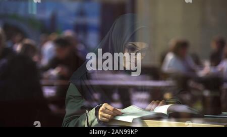 Young Arabic lady reading book in cafe, student preparing for exams, literature Stock Photo