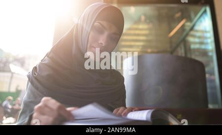 Motivated Muslim female student reading book in cafe modern education literature Stock Photo