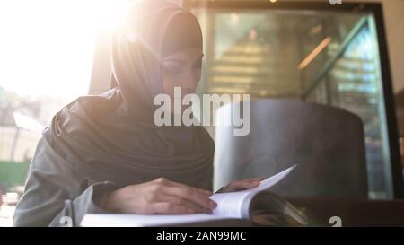 Self-confident Arabic lady reading book in cafe, education and self-development Stock Photo