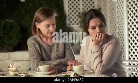 Young lady comforting upset friend, having coffee on terrace, friendship support Stock Photo