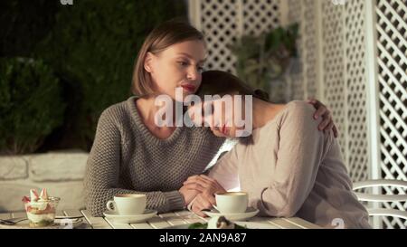 Young woman hugging sad female friend, sitting outside on terrace, friendship Stock Photo