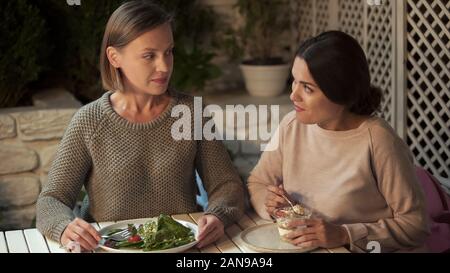 Female eating vegan salad, friend prefers creamy dessert, choosing nutrition Stock Photo