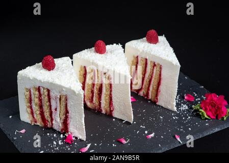Elegant Cake with coconut and raspberry covered with chocolate glaze. Slice of white layered cake on isolated black background. Wallpaper for pastry Stock Photo