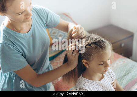 Mother brushes long blond hair of her daughter on the bed Stock Photo