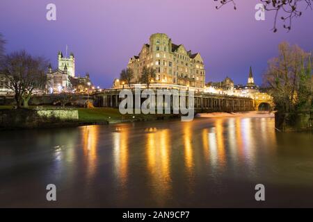 View across the River Avon to The Empire Hotel and Bath Abbey floodlit at dusk, Bath, Somerset, England, United Kingdom, Europe