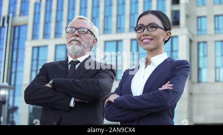 Confident aged and young business partners with crossed arms near office center Stock Photo
