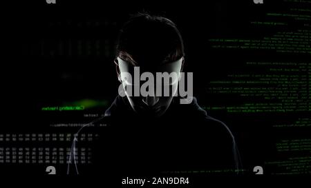 Scary hacker in white mask attacking personal data, codes and numbers background Stock Photo