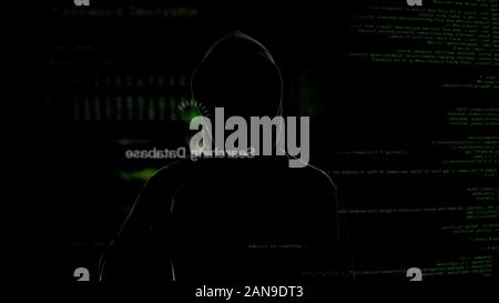 Anonymous hacker looking at virtual screen, stealing secret data, cyber crime Stock Photo