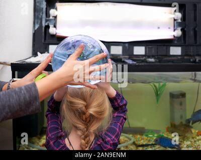 A little girl pouring fresh water from a heavy bottle in aquarium with a help of mother, indoor shot Stock Photo