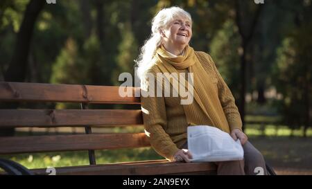 Happy old woman reading newspaper, sitting on bench in park, retirement age Stock Photo