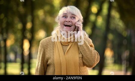 Smiling old woman talking on mobile phone in park, full family and friends Stock Photo