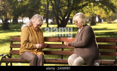 Couple of adult ladies playing cards sitting on bench in park, leisure activity Stock Photo