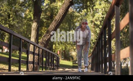 Sportive senior lady holding her knee feeling sharp pain during jogging, health Stock Photo