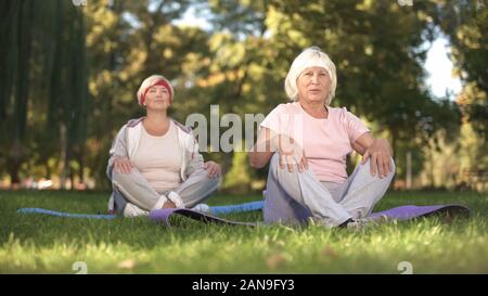 Senior women doing breezing exercises sitting in lotus position in park, energy Stock Photo