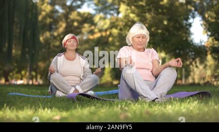 Elder women sitting in lotus position and meditating doing yoga in park, energy Stock Photo