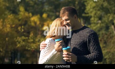Young couple having coffee break in park, holding hot drinks and hugging, love Stock Photo
