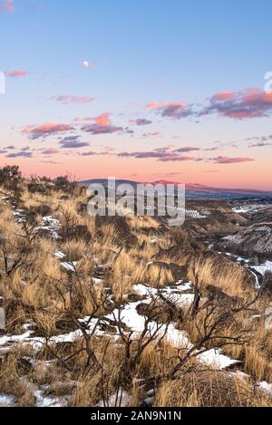 Colorful sunset over a snow covered vineyard in eastern washington with rocks and grasses in the foreground and mountains in the distance Stock Photo
