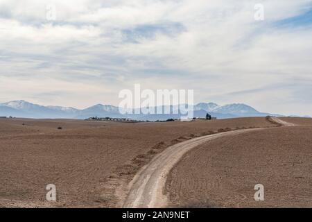 Dirt road through Agafay desert leading to Atlas Mountains, Morocco Stock Photo