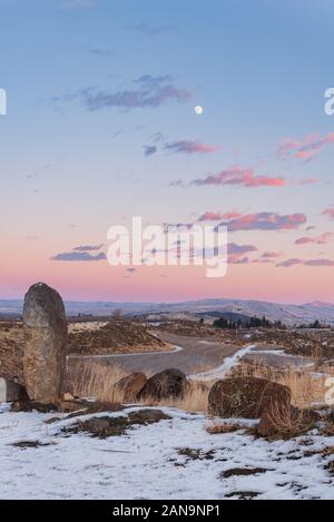 Colorful sunset over a snow covered vineyard in eastern washington with rocks and grasses in the foreground and mountains in the distance Stock Photo
