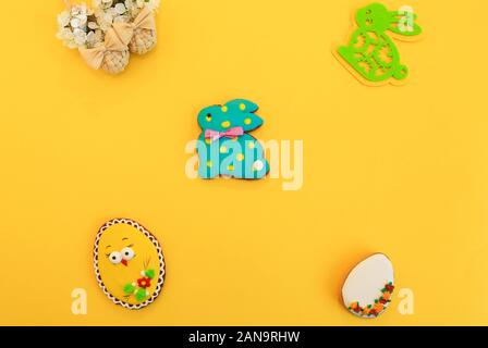 Handmade multi-colored gingerbread cookies in the form of a bunny and Easter eggs, straw shoes and flowers on a yellow background. Gingerbread Easter Stock Photo