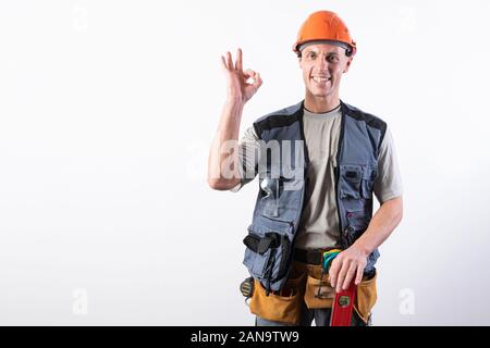 The builder shows the sign okay. In work clothes and hard hat. On a light gray background. Stock Photo