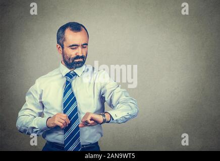 Calm middle-aged man looking at his wristwatch attentively, checking the time to not be late to a meeting. Mixed race bearded model isolated on gray b Stock Photo