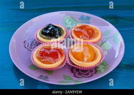 Punnets of dough filled in with various candied fruits, served in pink glass plate on blue wooden table Stock Photo