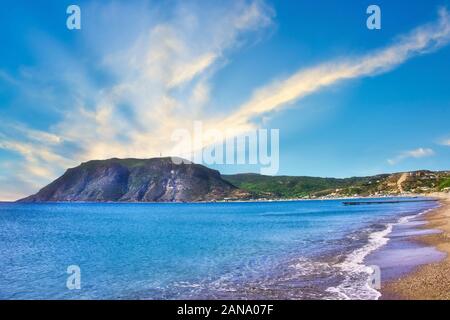 Horizontal photo with view on rock in Agios Stefanos Bay beach on famous Greek Kos island. Sky is blue with few clouds. Beach sandy with small stones. Stock Photo