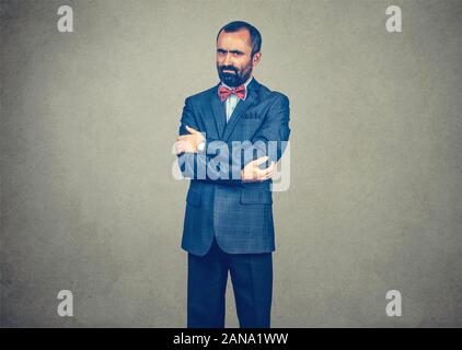 Businessman, man in suit standing looking serious cranky arms crossed. Mixed race bearded model isolated on gray studio wall background with copy spac Stock Photo