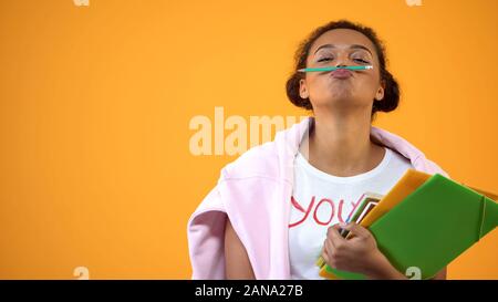 Positive african teenager holding pencil between nose and lips, mustache joke Stock Photo