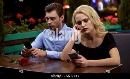 Two young people boring on date, using smartphones, problems in relationship Stock Photo