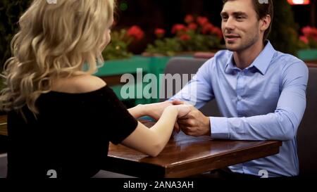 Young loving couple holding hands in cozy restaurant enjoying romantic date Stock Photo