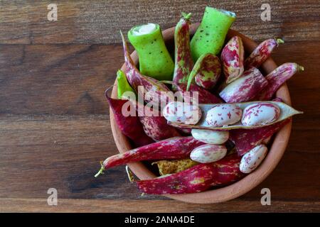 Pots and grains of young red and colorful organic beans in a clay bowl on dark wooden table, view from above Stock Photo