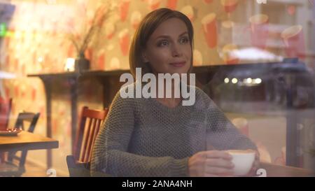 Thoughtful woman watching passersby through window of her favorite coffee house Stock Photo