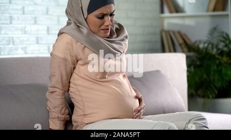 Pregnant woman in hijab feeling belly pain, risk of misbirth, prenatal care Stock Photo