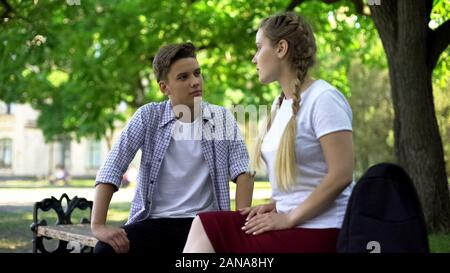 Teenagers couple conflicting, sitting at park bench, conflict based on jealousy Stock Photo