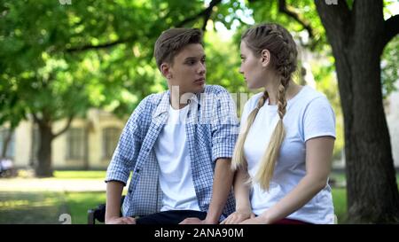 Two conflicting teenagers looking at each other, sitting on park bench, crisis Stock Photo
