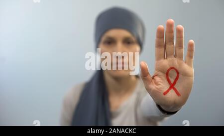 Red ribbon sign on womans palm showing stop gesture, AIDS awareness campaign Stock Photo