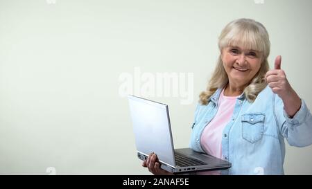 Aged lady using laptop showing thumbs-up, computer literacy for pensioners Stock Photo