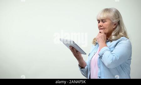 Thoughtful elderly lady using tablet, online banking app, modern technologies Stock Photo