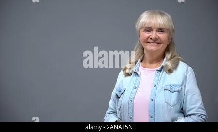 Positive elderly lady in casual clothes isolated on gray, happy secure old age Stock Photo