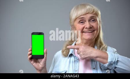 Smiling elderly woman showing smartphone with green screen, advertisement Stock Photo