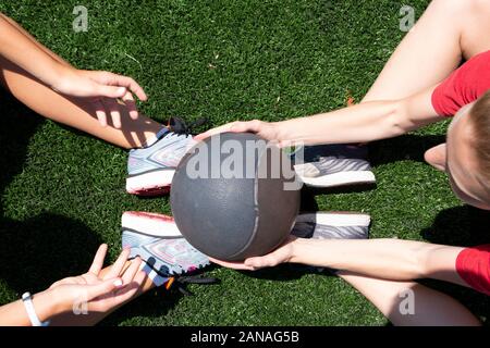 Two high school girls are passing a medicine ball while doing situps on a green turf field. Stock Photo