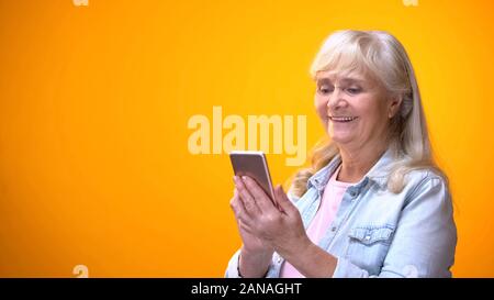 Happy elderly lady using smartphone, searching online medical service, shopping Stock Photo