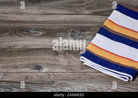 Top view of a striped and colorful dish towel on wooden planks with texture and wood grain. Abstract and structured background Stock Photo